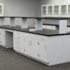 Angled view of white 16' x 4 ' laboratory cabinets island. Center shelf centered across black countertop.